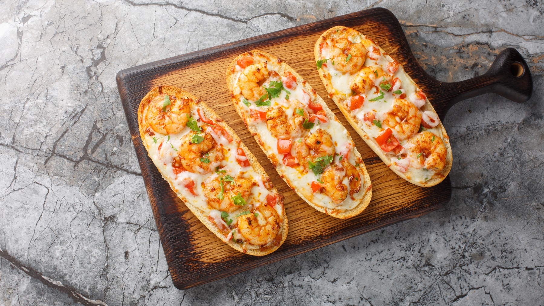 Überbackenes Baguette mit Garnelen auf einem Holzbrett von oben fotografiert.