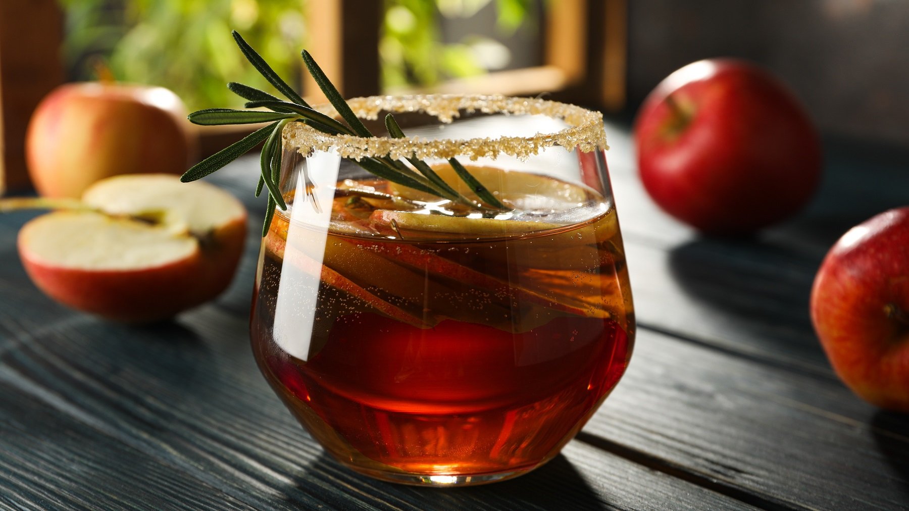 Ein Glas mit dem herbstlichen Aperol Spritz auf einem dunklen Holztisch von der Seite fotografiert.