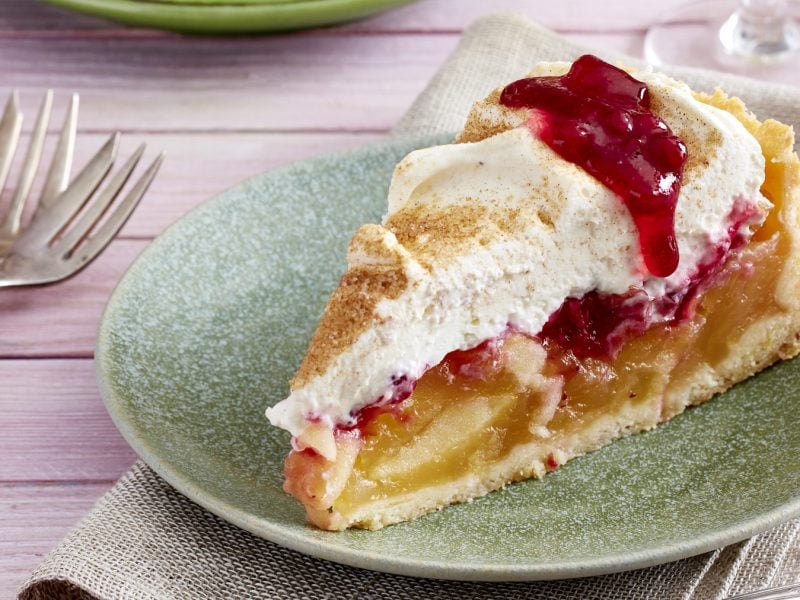 Ein Stück vom Kuchen auf einem grünen Teller und fliederfarbenen Tisch mit zwei kleinen Kuchengabeln. Alles von der Seite fotografiert.