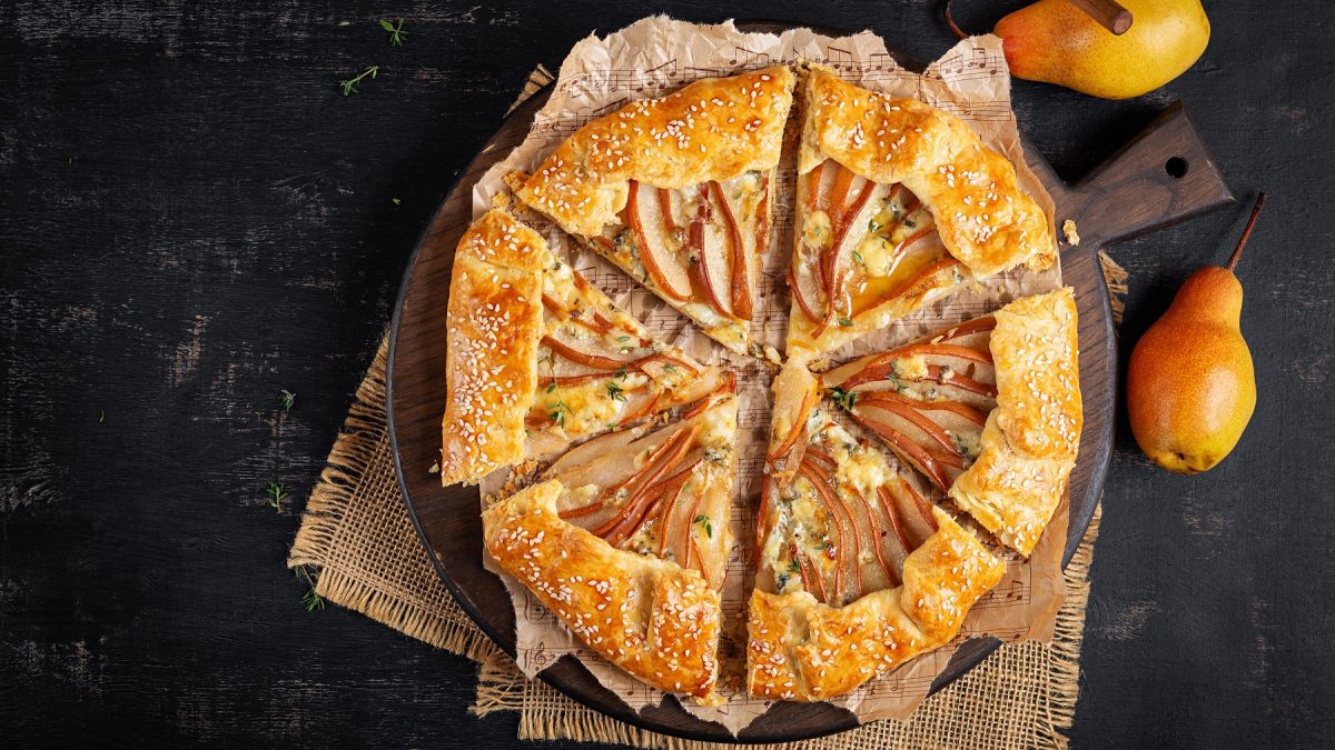 Angeschniettene Birnen-Ziegenkäse Galette mit Sesamsamen von oben fotografiert, daneben frische Birnen.