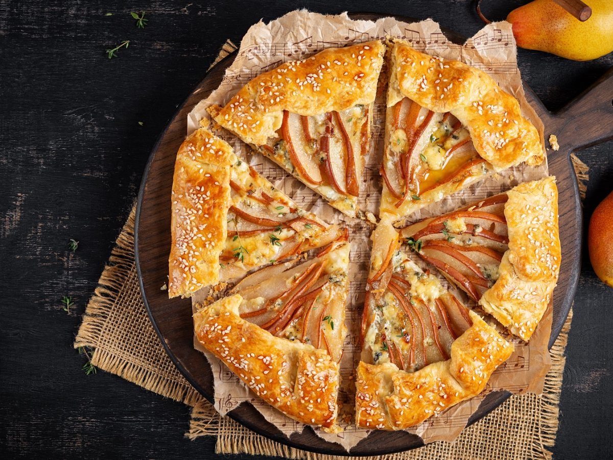 Angeschniettene Birnen-Ziegenkäse Galette mit Sesamsamen von oben fotografiert, daneben frische Birnen.