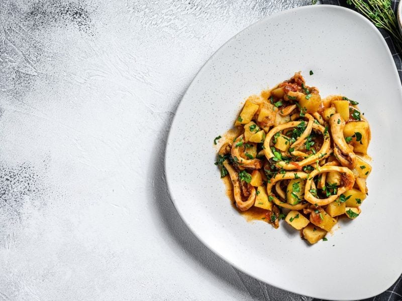 Calamari e patate auf einem weißen teller von oben fotografiert. Daneben Geschirrtuch mit Besteck.