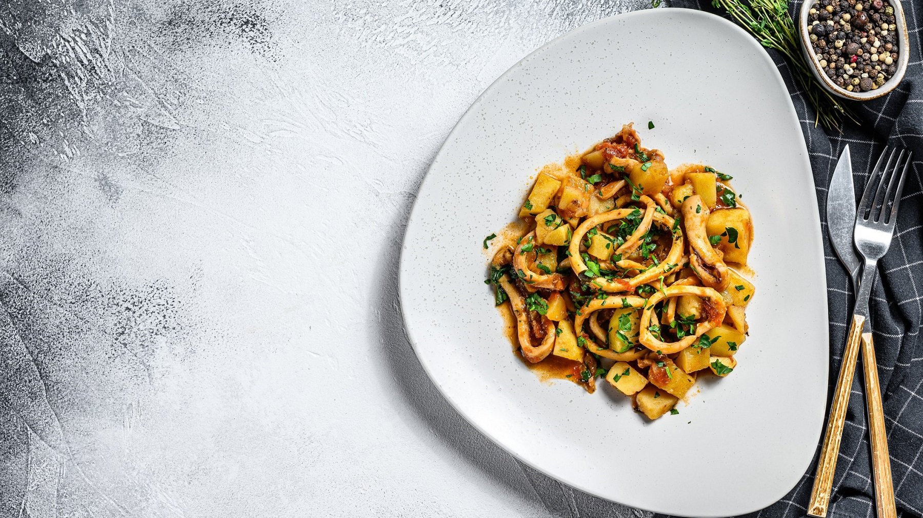 Calamari e patate auf einem weißen teller von oben fotografiert. Daneben Geschirrtuch mit Besteck.