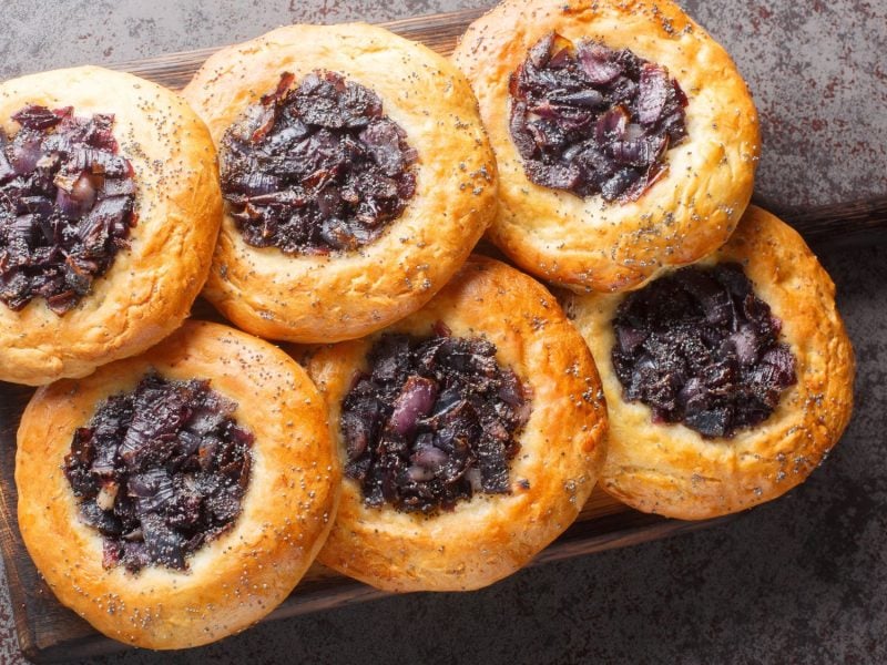 Frische, goldbraune Zwiebelkuchen "Cebularz" mit Mohn auf Holzbrett angerichtet, der Boden zeigt eine rustikale Tischplatte.