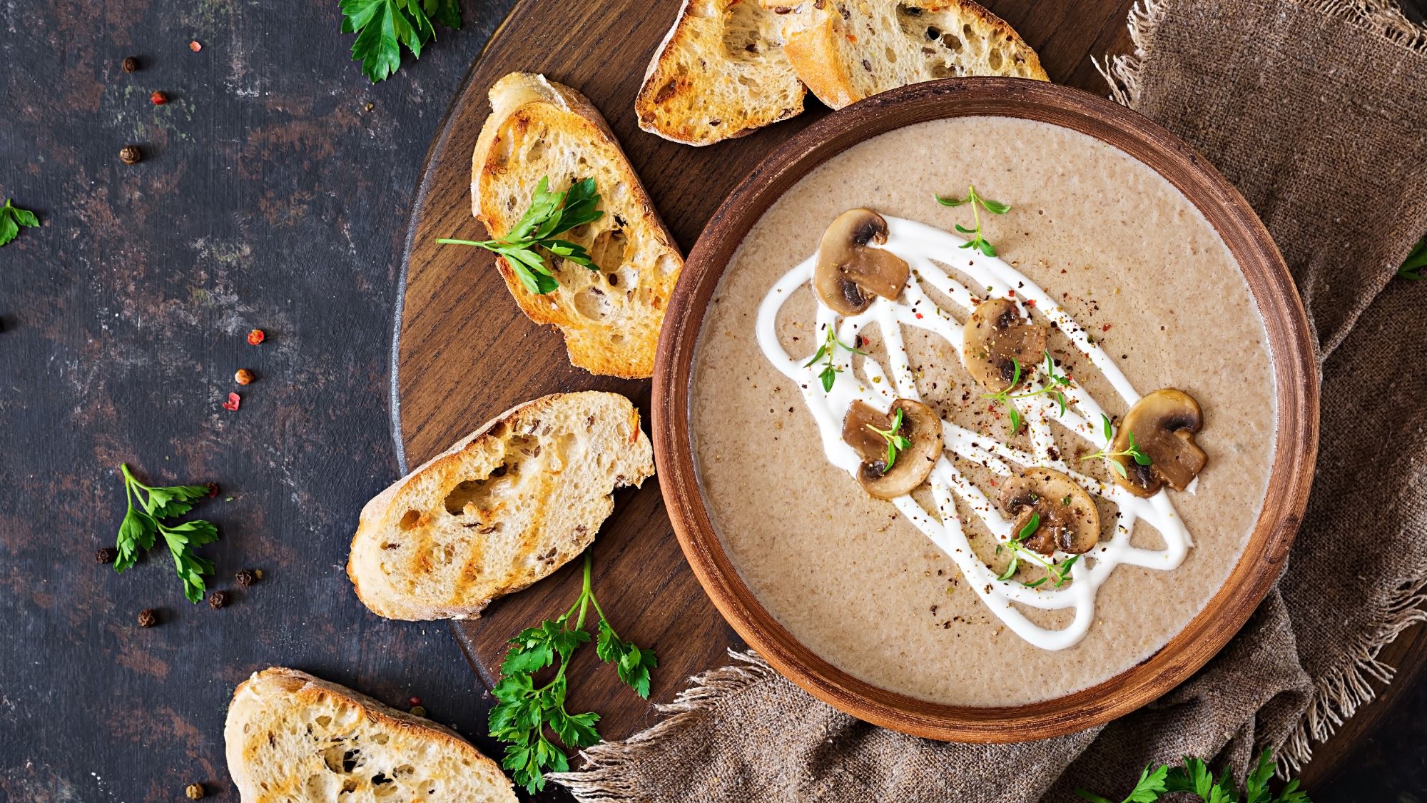 Cremige Champignoncremesuppe mit Sahnedekor, frischen Kräutern und gebratenen Champignons, serviert mit gerösteten Brotscheiben.