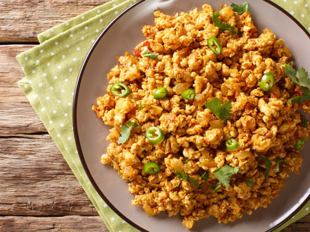 Ein Teller mit Chicken Keema, dekoriert mit grünen Chilischeiben und Koriander auf einer grünen Serviette.