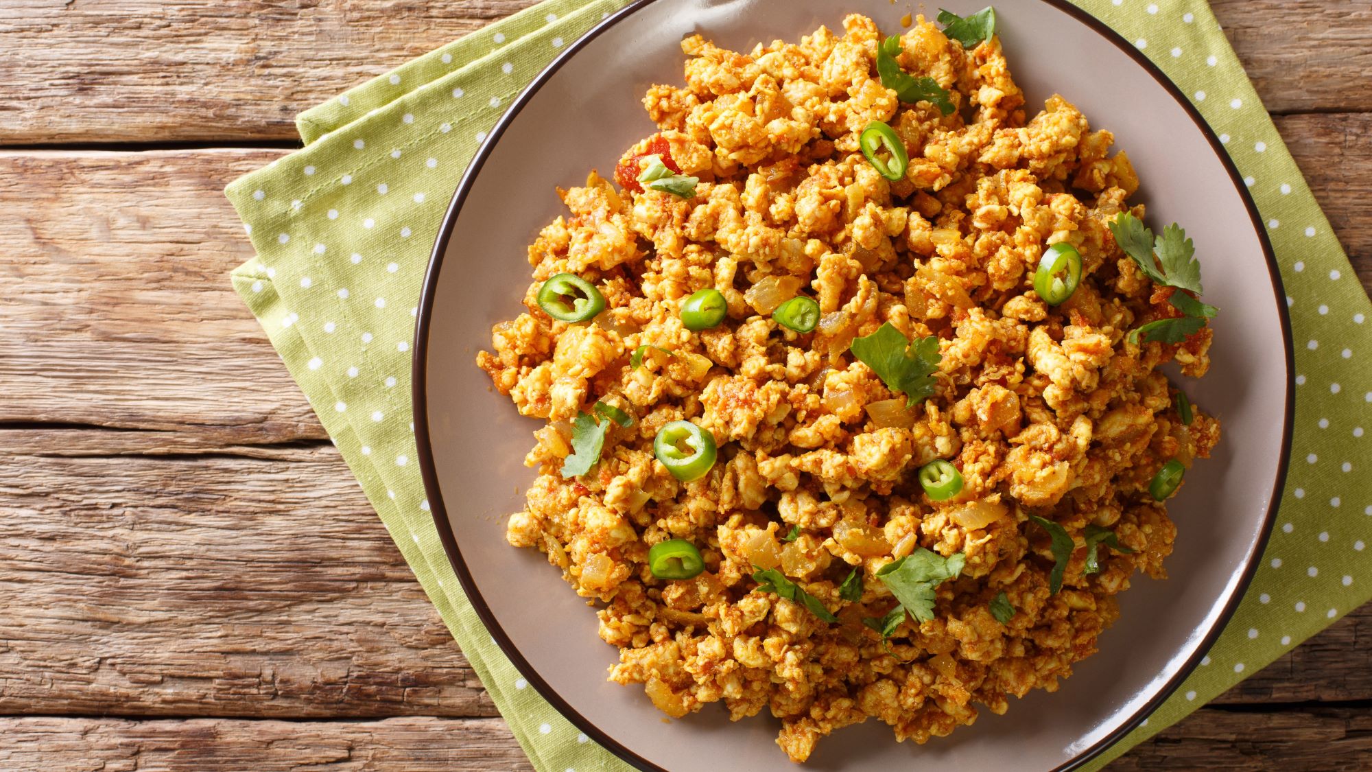 Ein Teller mit Chicken Keema, dekoriert mit grünen Chilischeiben und Koriander auf einer grünen Serviette.