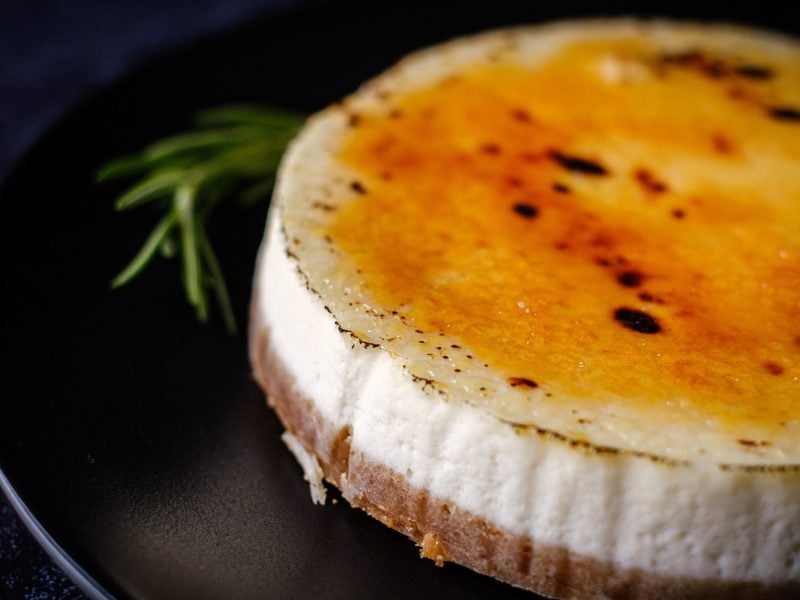 Der Crème brûlée Cheesecake auf einem schwarzen Teller und dunkelblauem Untergrund.