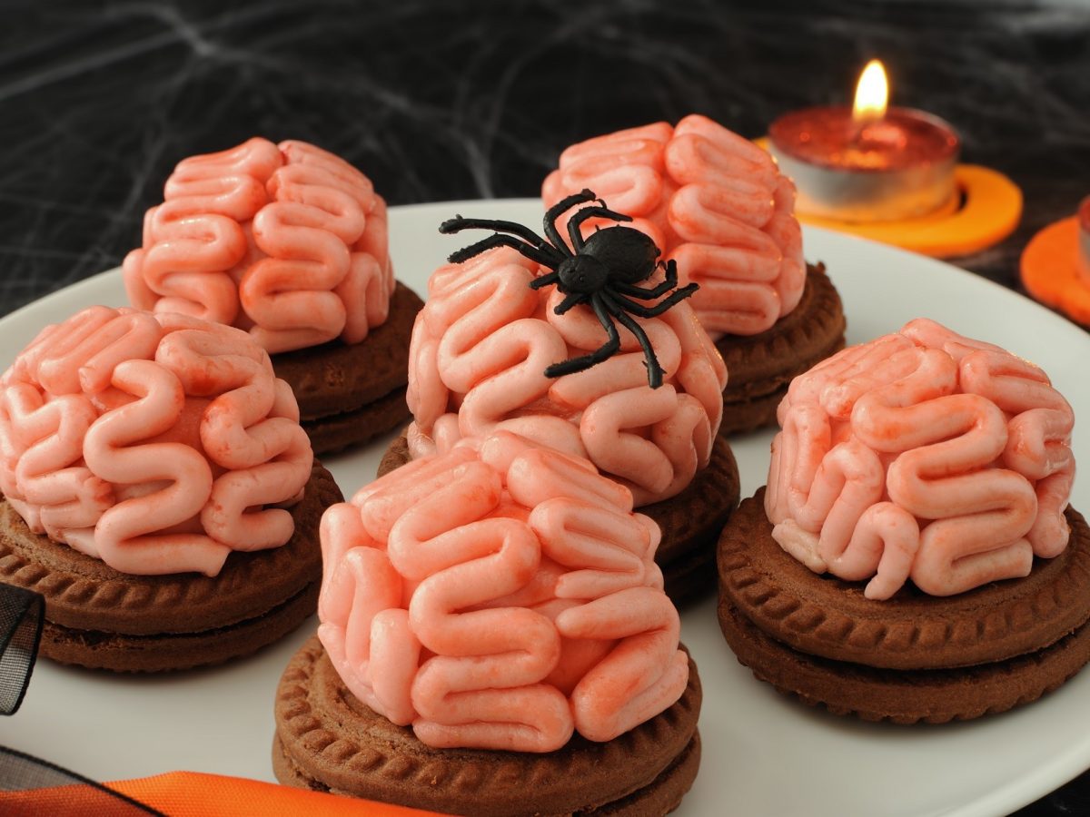 Draufsicht, schräg: Sechs Halloweenkekse auf einem weißem Teller. Die Die Brain-Cookies stehen in einem Halloween-mäßig dekorierten Umfeld.