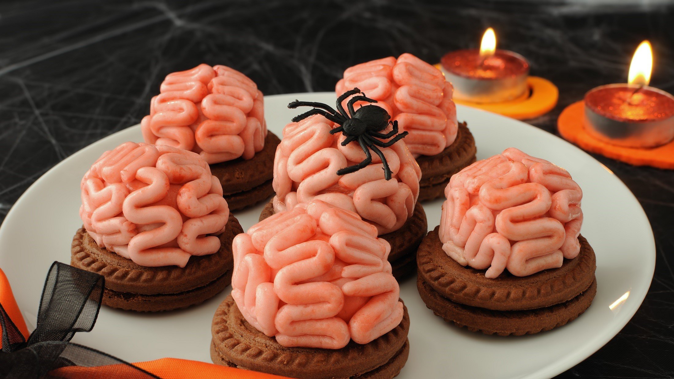 Draufsicht, schräg: Sechs Halloweenkekse auf einem weißem Teller. Die Die Brain-Cookies stehen in einem Halloween-mäßig dekorierten Umfeld.