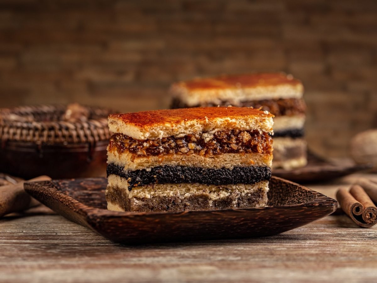 Zwei Stücke Flódni bzw., Fächertorte von vorne fotografiert. Daneben Zimtstangen und Walnüsse.