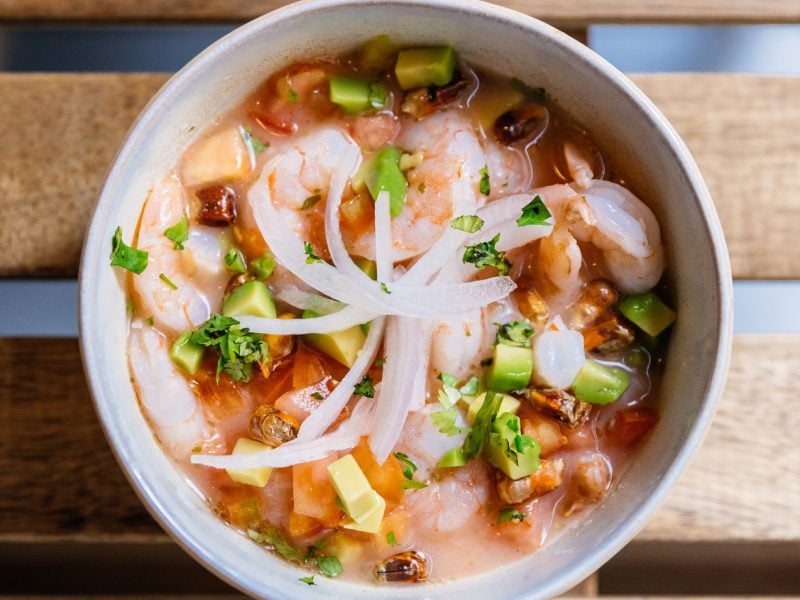 Eine weiße Schüssel mit dem Garnelen-Ceviche auf einem Holztisch. Alles direkt von oben fotografiert.