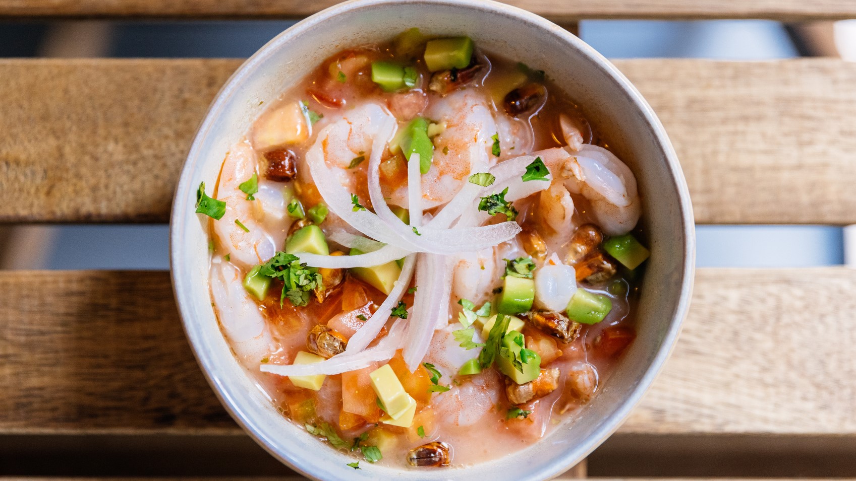 Eine weiße Schüssel mit dem Garnelen-Ceviche auf einem Holztisch. Alles direkt von oben fotografiert.