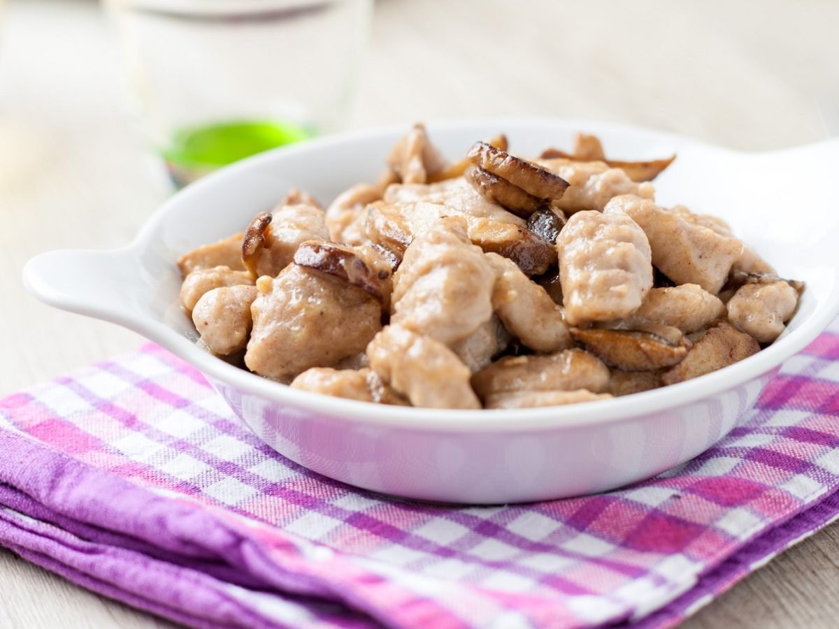 Gnocchi di castagne mit Steinpilzen in einer weißen Schale auf einem lila Geschirrtuch von schräg oben fotografiert.