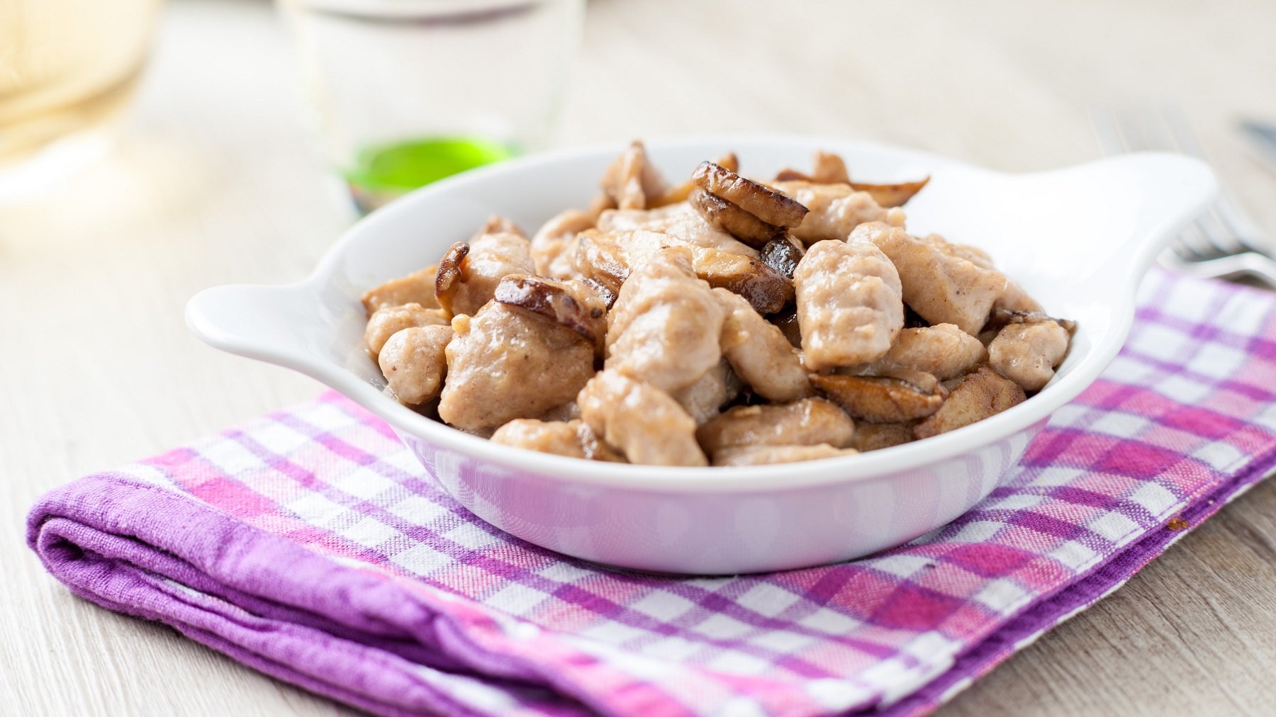 Gnocchi di castagne mit Steinpilzen in einer weißen Schale auf einem lila Geschirrtuch von schräg oben fotografiert.