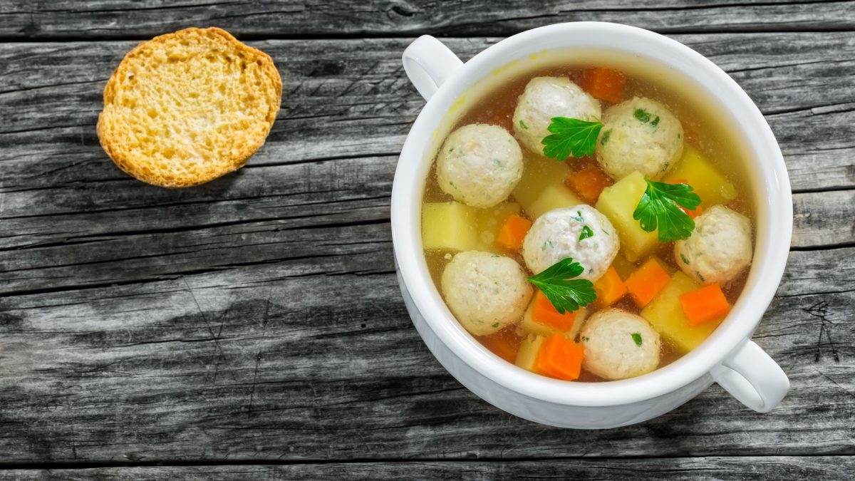 Hochzeitssuppe mit Karotten und Kartoffeln, garniert mit Petersilie, in einer weißen Schale, daneben ein Zwieback.