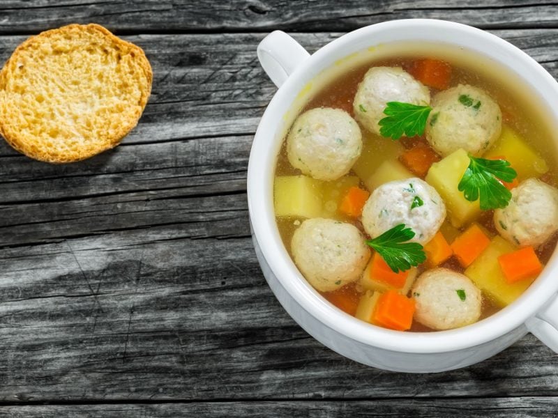 Hochzeitssuppe mit Karotten und Kartoffeln, garniert mit Petersilie, in einer weißen Schale, daneben ein Zwieback.