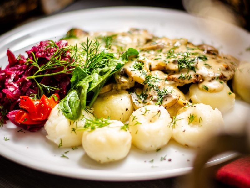 Teller mit schlesischen Kartoffelklößen "Kluski śląskie", überzogen mit Pilzsoße und frischem Dill, dazu Rote Bete Salat und Spinatblätter.