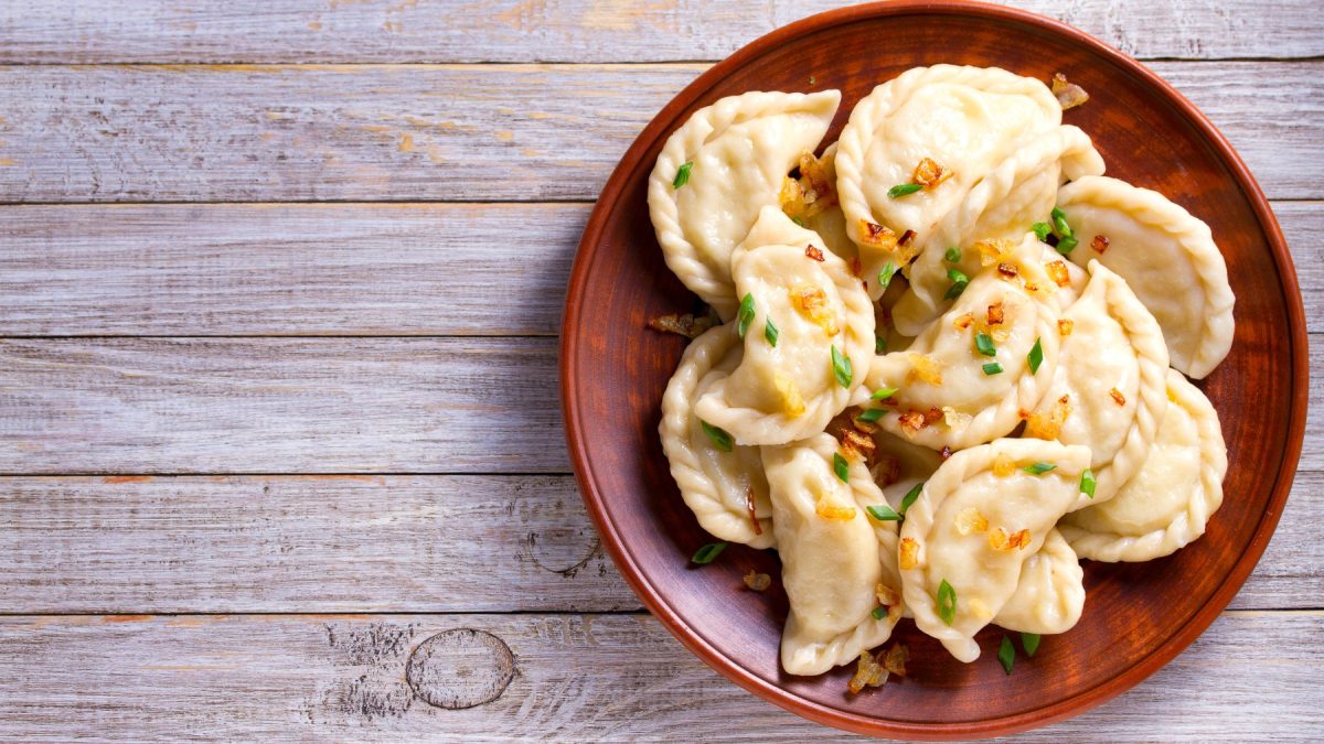 Kürbis-Curry-Dumplings auf einem braunen Teller auf grauem Hintergrund.