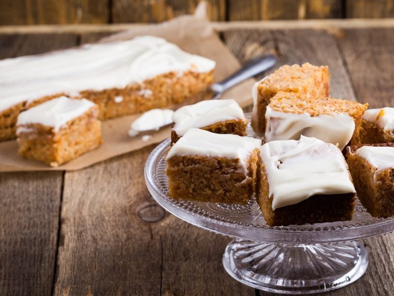 Eine Glasplatte mit einigen Stücken des Kuchens auf einem rustikalen Holztisch mit dem Blech und Kuchen im Hintergrund.