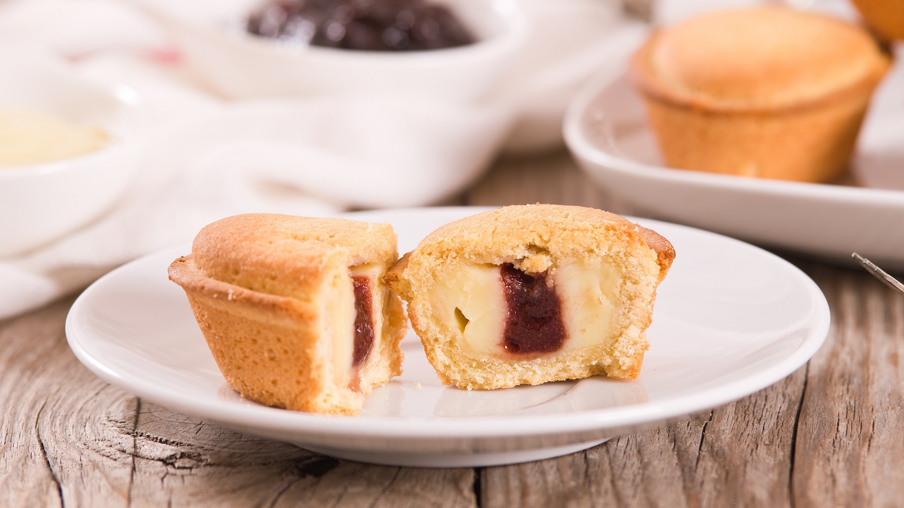 Angeschnittener Pasticciotto napoletano auf einem weißen Teller von vorne fotografiert.