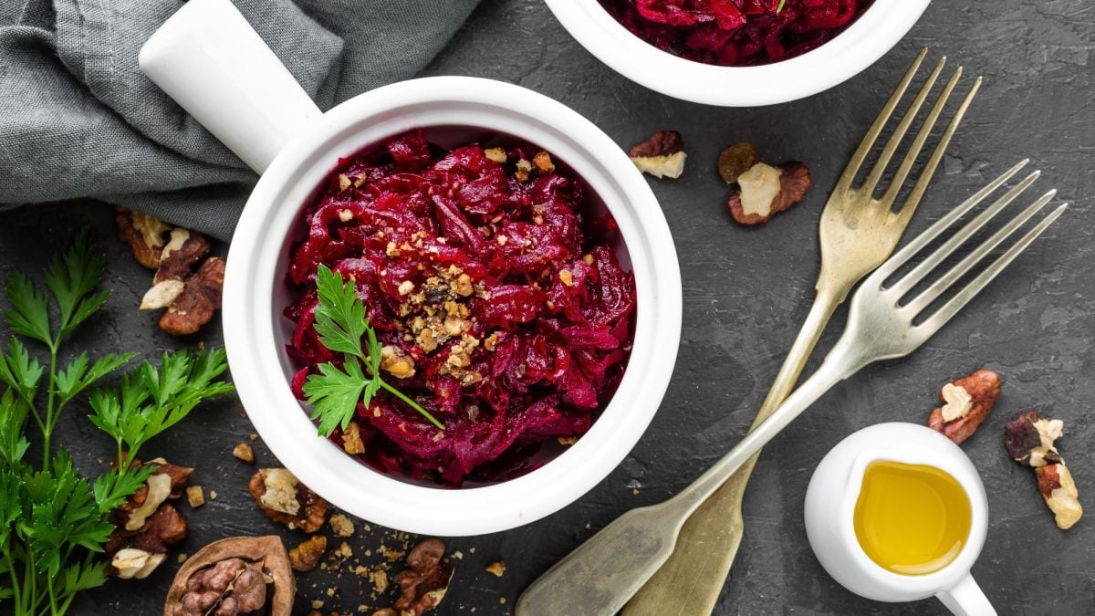 Rote-Bete-Salat mit gehackten Walnüssen und Petersilie in einer weißen Schale, dekoriert mit Gabeln und Walnüssen auf dunklem Schiefer.