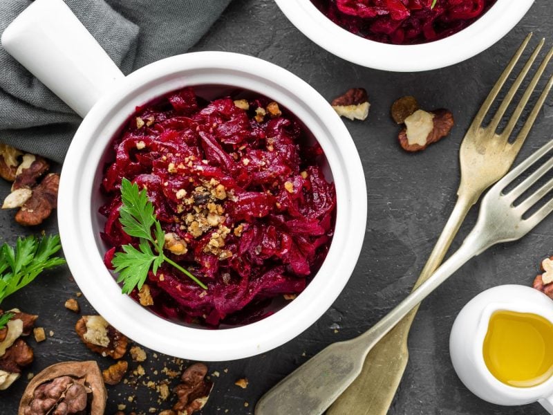 Rote-Bete-Salat mit gehackten Walnüssen und Petersilie in einer weißen Schale, dekoriert mit Gabeln und Walnüssen auf dunklem Schiefer.