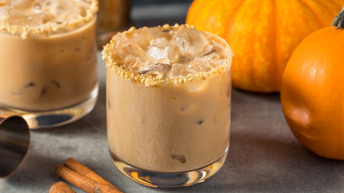 Pumpkin Spice White Russian mit Butterkeksrand in einem Glas, im Hintergrund Kürbisse.