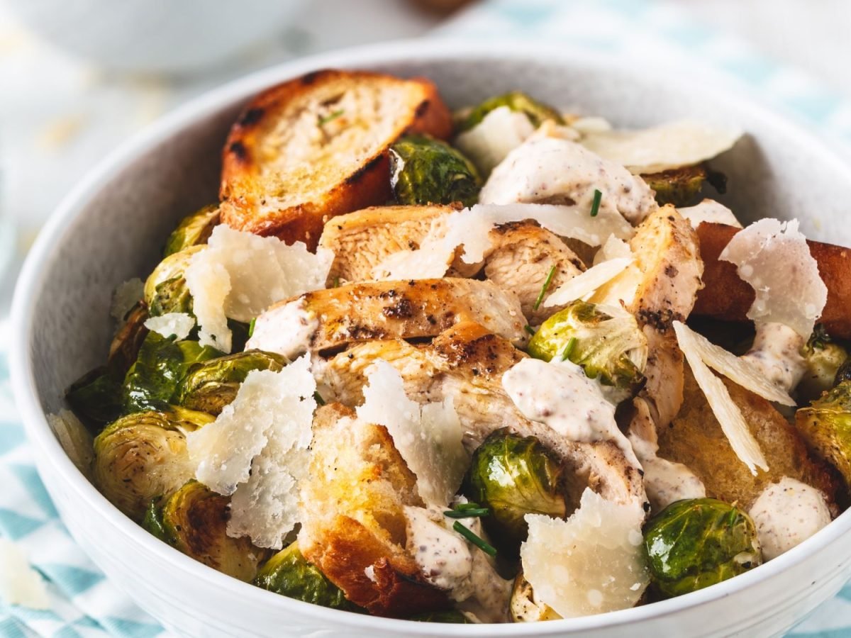 Frischer Caesar-Salat mit Rosenkohl, gegrilltem Hühnchen, knusprigen Croutons und Parmesan, serviert in einer weißen Schüssel