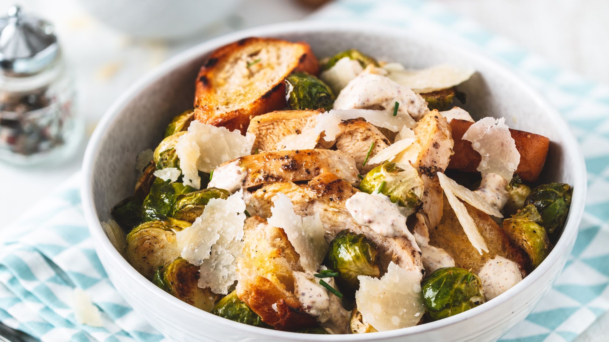 Frischer Caesar-Salat mit Rosenkohl, gegrilltem Hühnchen, knusprigen Croutons und Parmesan, serviert in einer weißen Schüssel