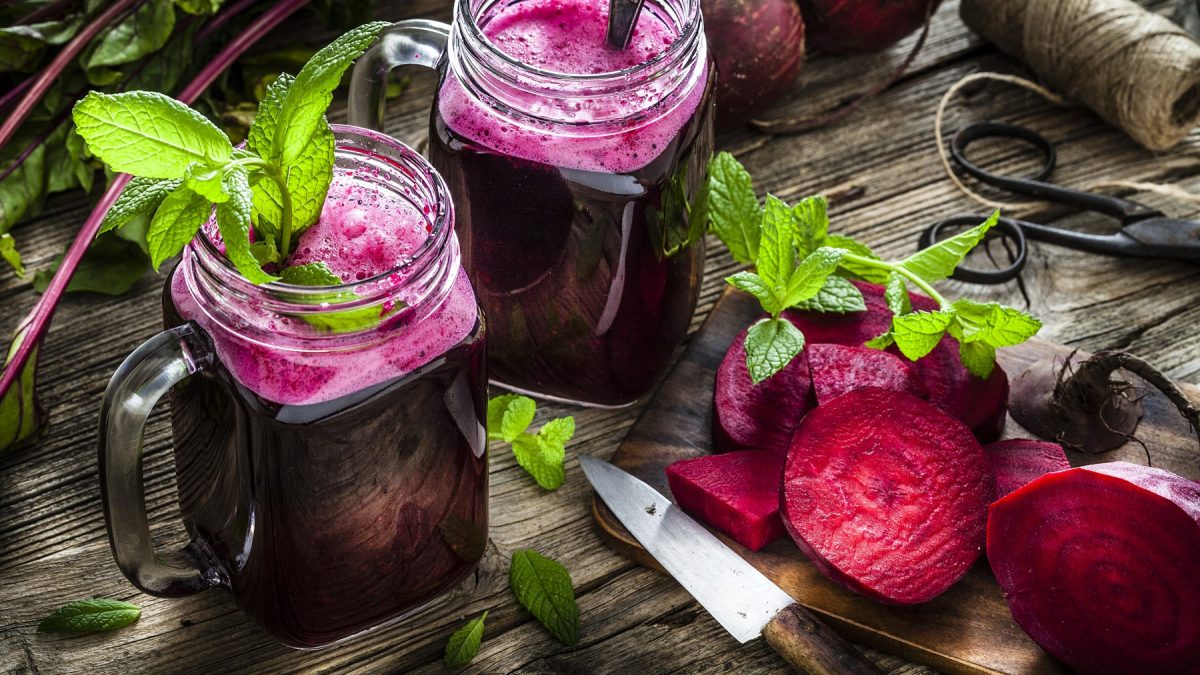 2 Gläser Rote Bete Smoothie auf hölzernem Hintergrund. Rechts auf dem Foto aufgeschnittene Rote Bete und Messer.