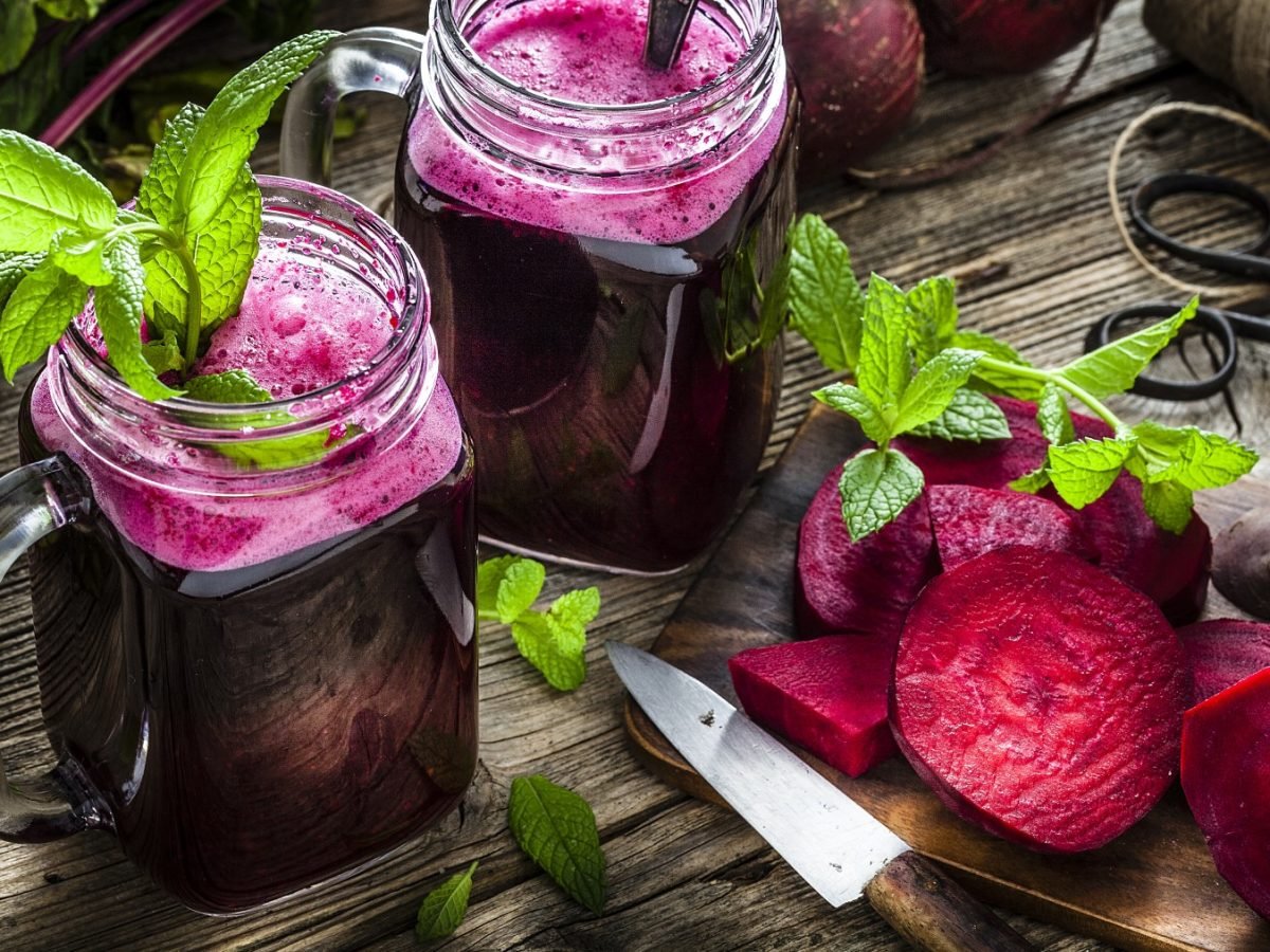 2 Gläser Rote Bete Smoothie auf hölzernem Hintergrund. Rechts auf dem Foto aufgeschnittene Rote Bete und Messer.