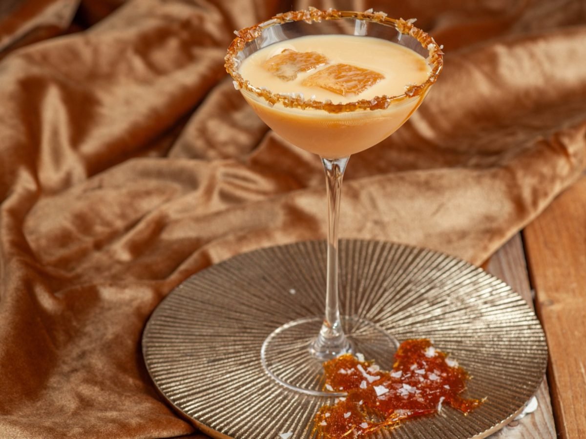 Salted Caramel Martini in einem martiniglas auf einem silbernen tablett mit Karamellstücken, daneben eine braune Samtdecke.