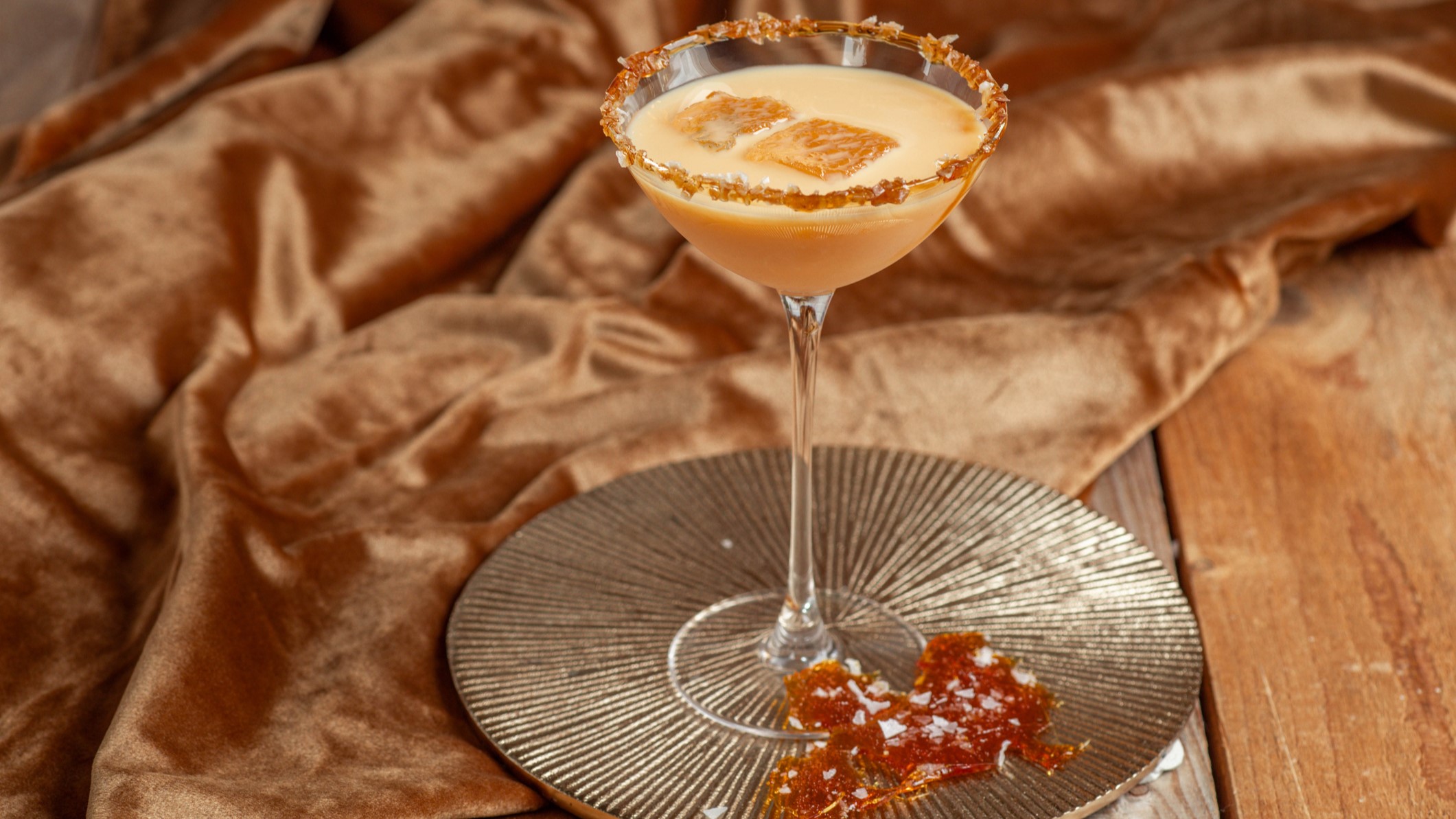 Salted Caramel Martini in einem martiniglas auf einem silbernen tablett mit Karamellstücken, daneben eine braune Samtdecke.