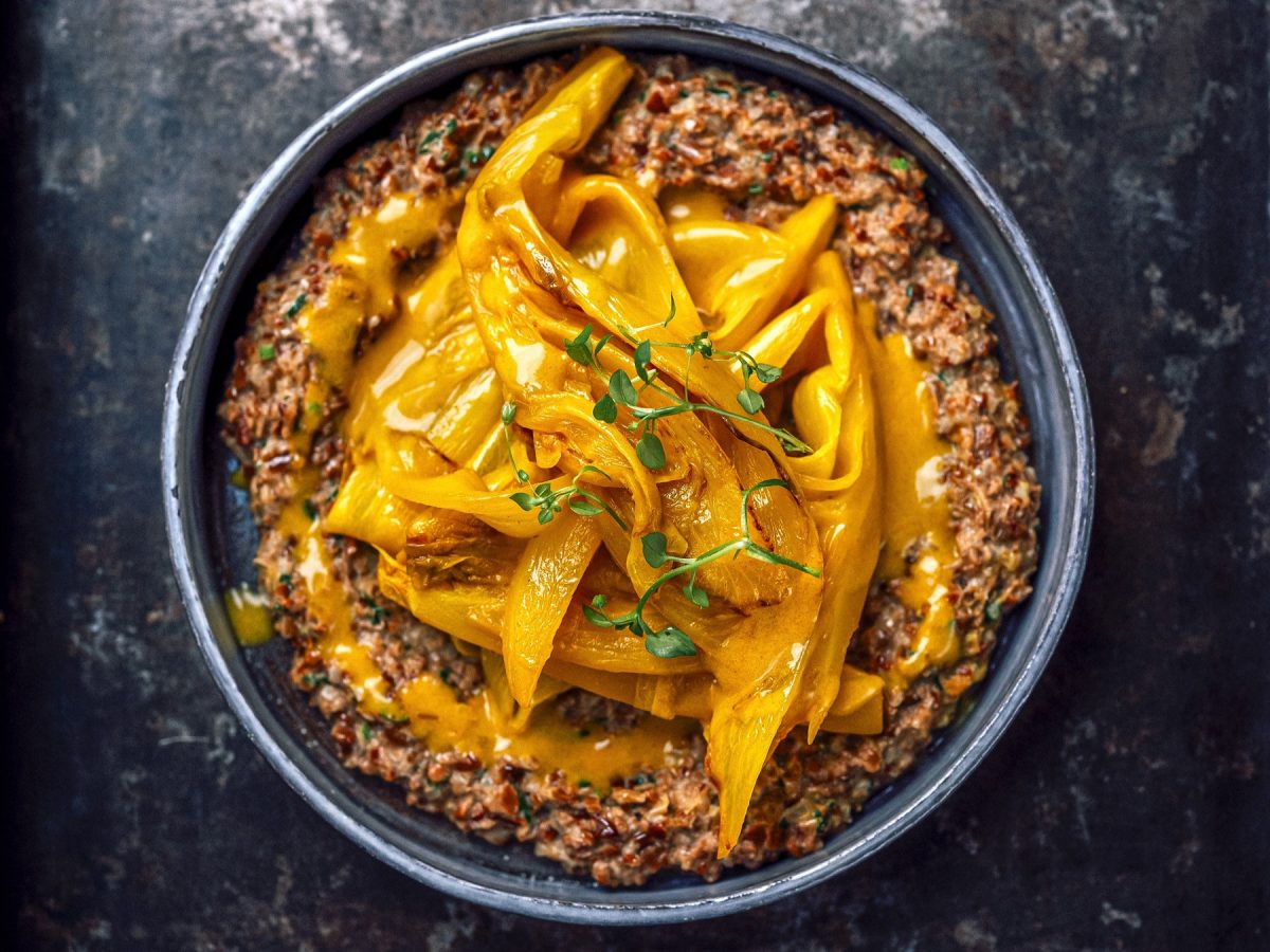 Ein grauer Teller mit dem Sonnenblumenkern-Risotto auf grauem Untergrund direkt von oben fotografiert.