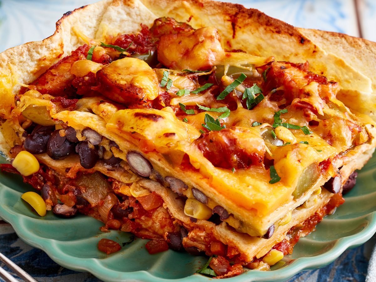 Tortilla-Hähnchen-Lasagne auf einem grünen Teller auf hellem Hintergrund.