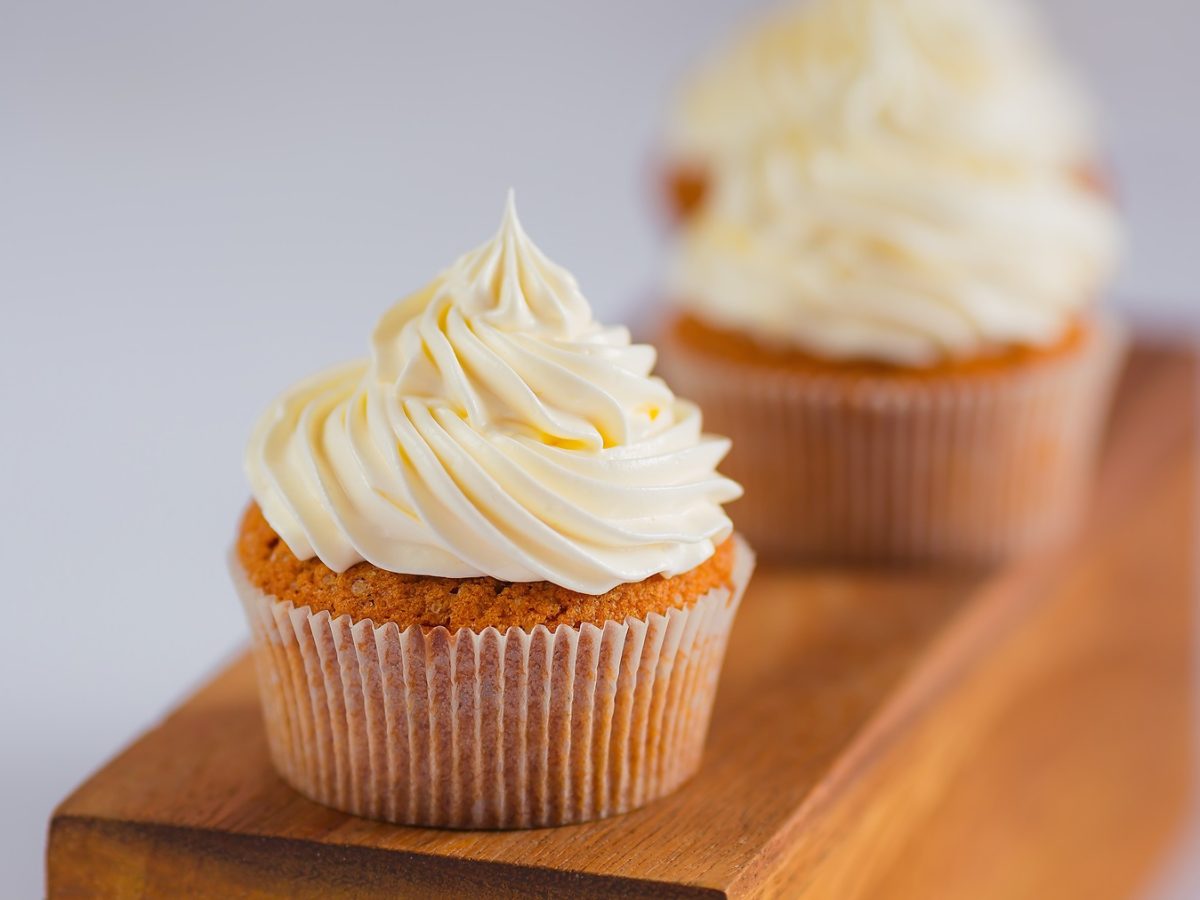 Cupcakes auf einem Holzbalken mit einfachem Frosting aus Buttercreme von vorne fotografiert.