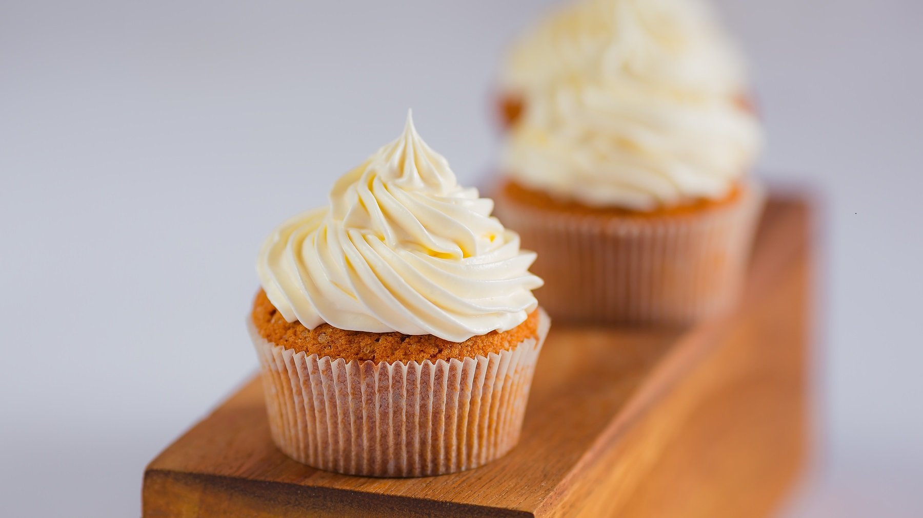 Cupcakes auf einem Holzbalken mit einfachem Frosting aus Buttercreme von vorne fotografiert.