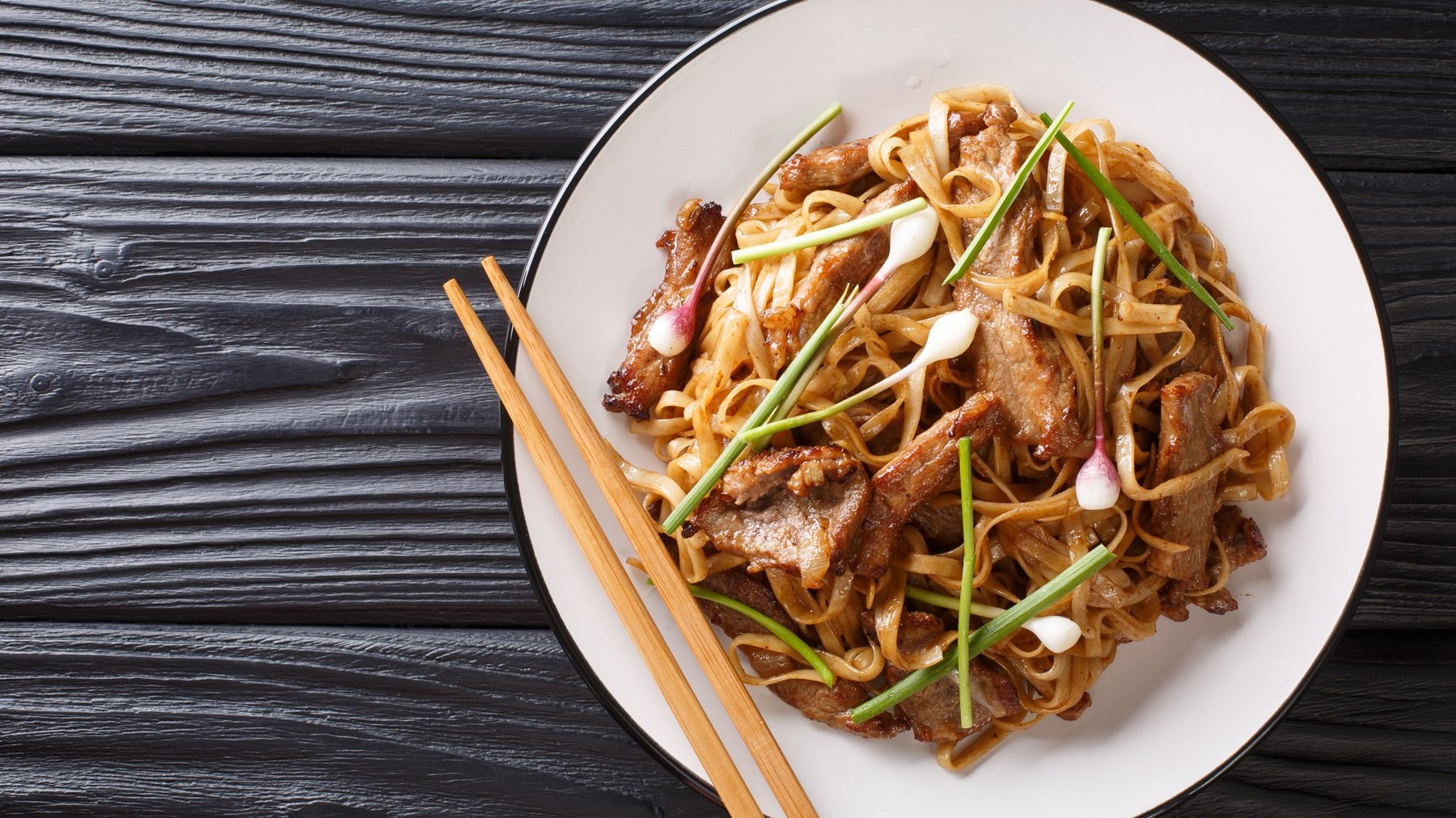 Ein weißer Teller mit dem Chow Fun auf einem schwarzen Holztisch.