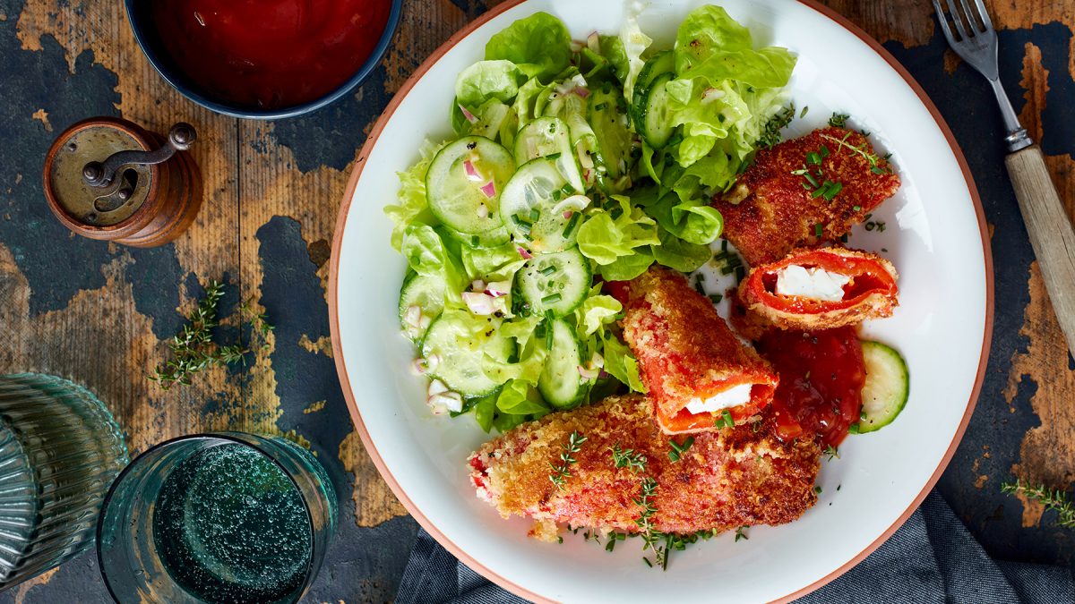 Feta-Paprika-Cordon-Bleu auf einem weißen Teller auf hölzernem Hintergrund.