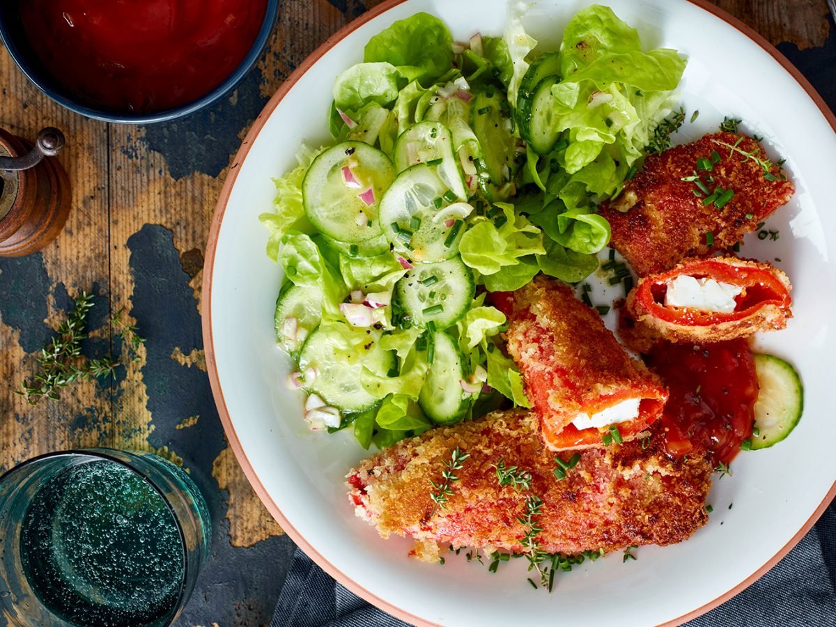 Feta-Paprika-Cordon-Bleu auf einem weißen Teller auf hölzernem Hintergrund.