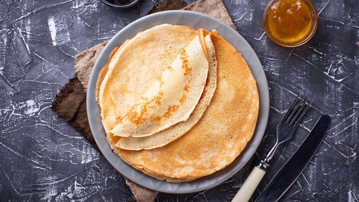 Crêpes auf einem Teller von oben fotografiert, daneben Besteck und ein Schälchen mit Marmelade.