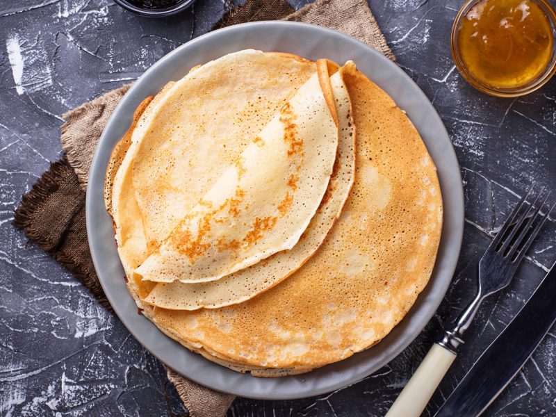 Crêpes auf einem Teller von oben fotografiert, daneben Besteck und ein Schälchen mit Marmelade.