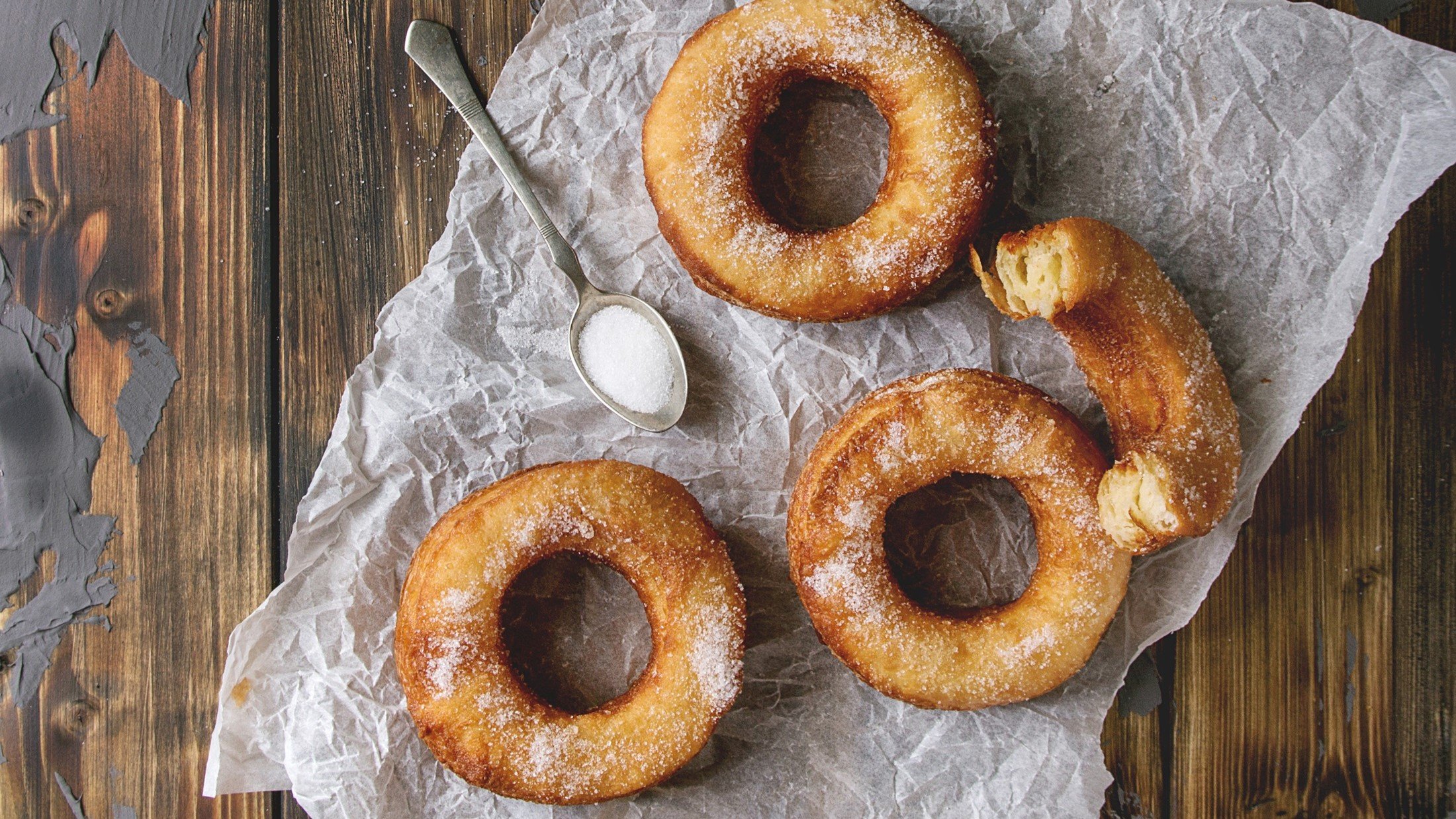 Draufsicht: Mehrere Cronuts auf einem hellen Papier, das auf einem Holzboden liegt.