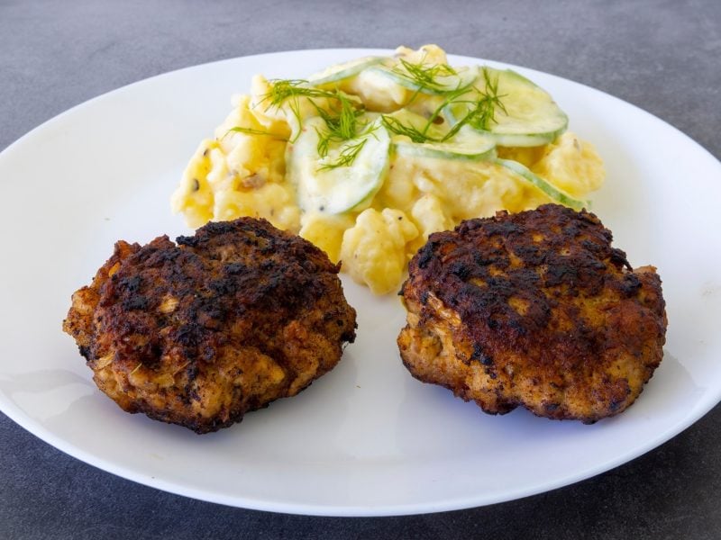 Berliner Buletten mit Kartoffelsalat und Gurken auf einem weißen Teller. Draufsicht schräg