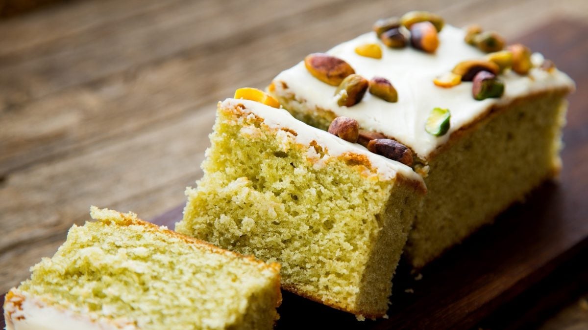 Pistazienkuchen mit Zucker-Zitronen-Glasur und Pistazienkernen-Deko, aufgeschnitten auf einem Untergrund aus rustikalem Holz.