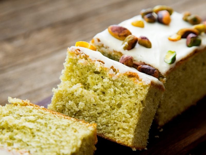 Pistazienkuchen mit Zucker-Zitronen-Glasur und Pistazienkernen-Deko, aufgeschnitten auf einem Untergrund aus rustikalem Holz.