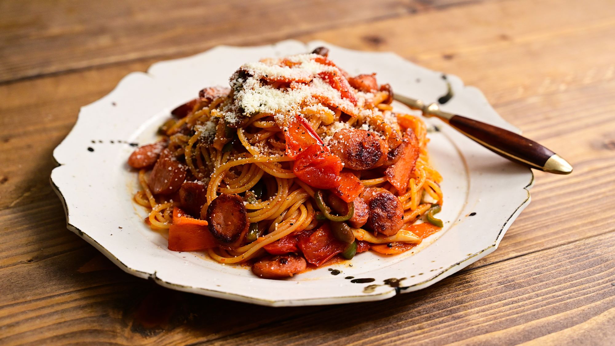 Ein Teller mit Spaghetti mit istrischem Wurstgulasch serviert auf rustikalem Holztisch mit weißem Randteller.