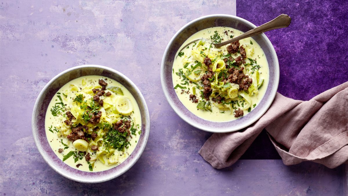 Draufsicht: Zwei Schüsselm mit Käse-Lauch-Bowl auf lila Untergrund.