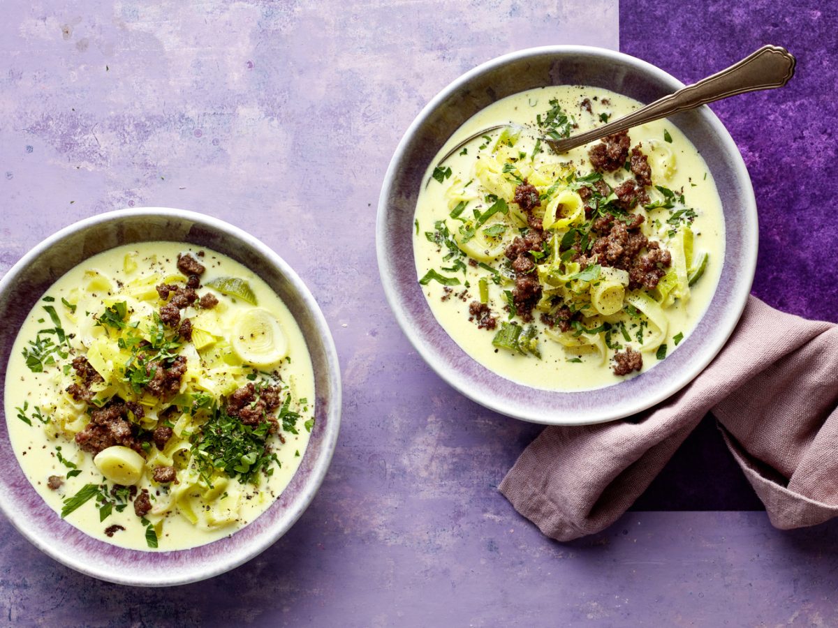 Draufsicht: Zwei Schüsselm mit Käse-Lauch-Bowl auf lila Untergrund.